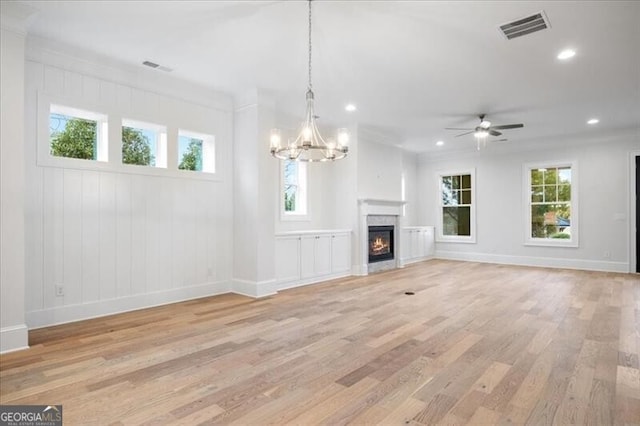 unfurnished living room featuring ceiling fan with notable chandelier, a healthy amount of sunlight, and light hardwood / wood-style floors