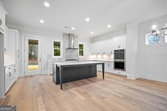 kitchen featuring wall chimney exhaust hood, light hardwood / wood-style flooring, a kitchen breakfast bar, stainless steel double oven, and white cabinets