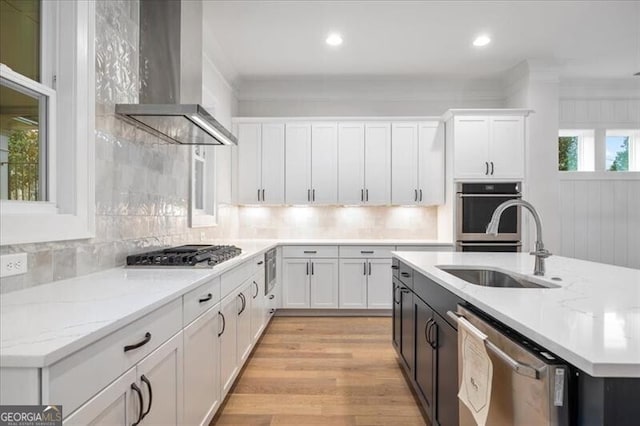 kitchen featuring wall chimney range hood, light stone countertops, white cabinets, and appliances with stainless steel finishes