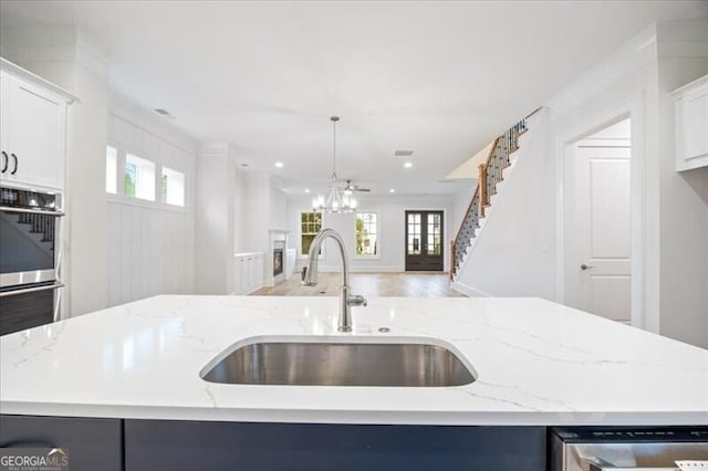 kitchen featuring pendant lighting, sink, a kitchen island with sink, light stone counters, and an inviting chandelier