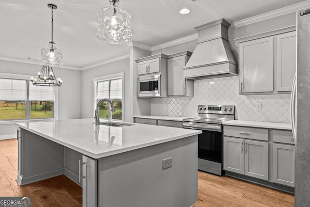 kitchen featuring sink, gray cabinets, premium range hood, stainless steel appliances, and a center island with sink