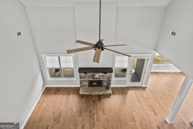 unfurnished living room featuring ceiling fan, a stone fireplace, hardwood / wood-style floors, and a high ceiling