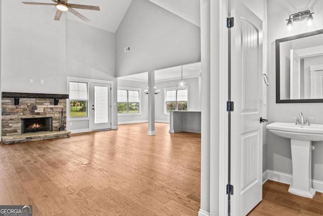 unfurnished living room with hardwood / wood-style flooring, high vaulted ceiling, a fireplace, and ceiling fan with notable chandelier