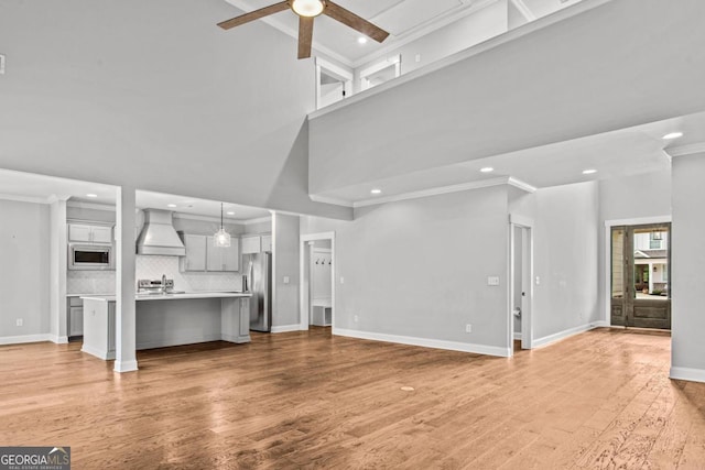 unfurnished living room with a high ceiling, crown molding, ceiling fan, and light hardwood / wood-style floors