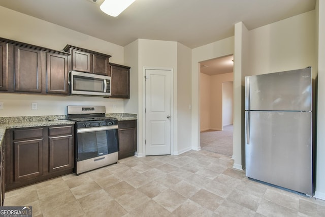 kitchen with appliances with stainless steel finishes, light stone counters, and dark brown cabinetry