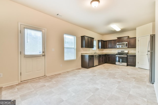 kitchen featuring stainless steel appliances, light stone counters, and dark brown cabinetry