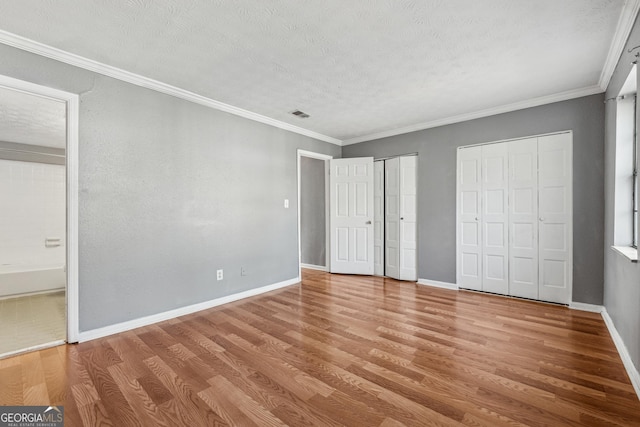 unfurnished bedroom with hardwood / wood-style flooring, crown molding, a textured ceiling, and two closets