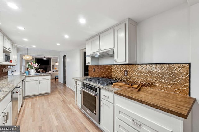 kitchen featuring appliances with stainless steel finishes, tasteful backsplash, white cabinets, kitchen peninsula, and light wood-type flooring