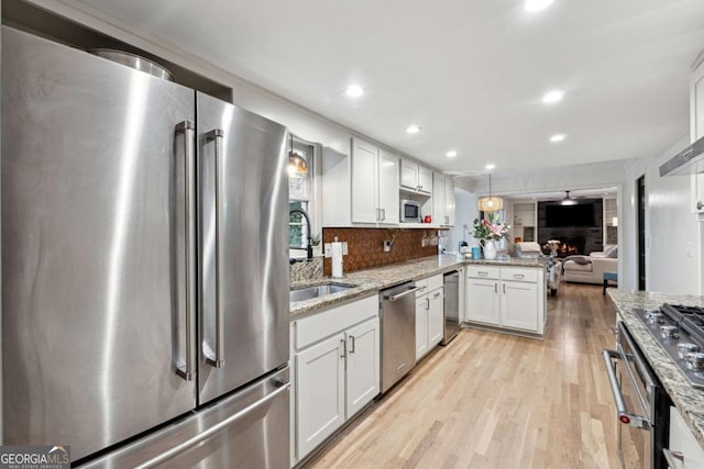 kitchen with sink, appliances with stainless steel finishes, light stone countertops, white cabinets, and kitchen peninsula