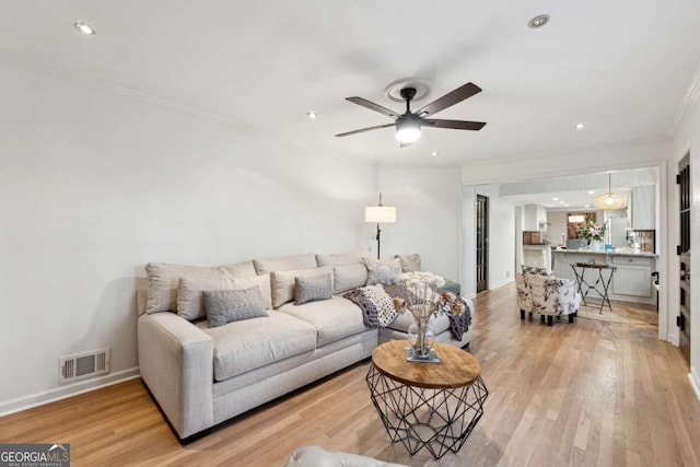 living room featuring light hardwood / wood-style flooring, ornamental molding, and ceiling fan