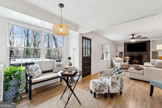 living room with crown molding, light hardwood / wood-style flooring, built in features, ceiling fan, and a fireplace