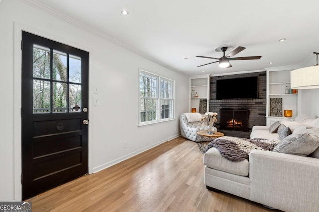 living room featuring crown molding, a fireplace, light hardwood / wood-style floors, and built in shelves