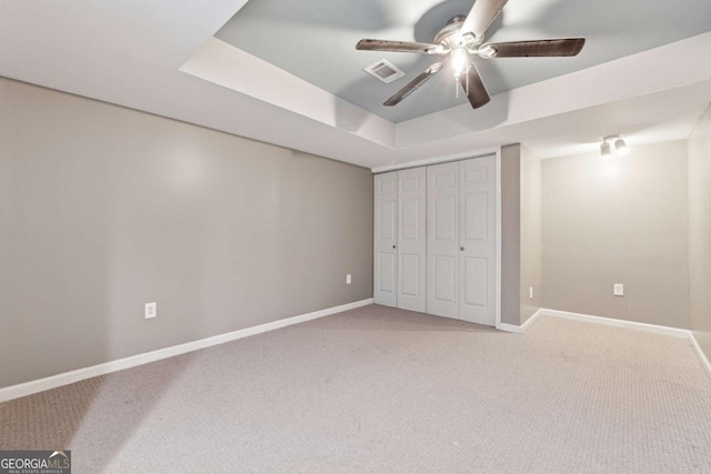 unfurnished bedroom featuring a tray ceiling, carpet floors, a closet, and ceiling fan