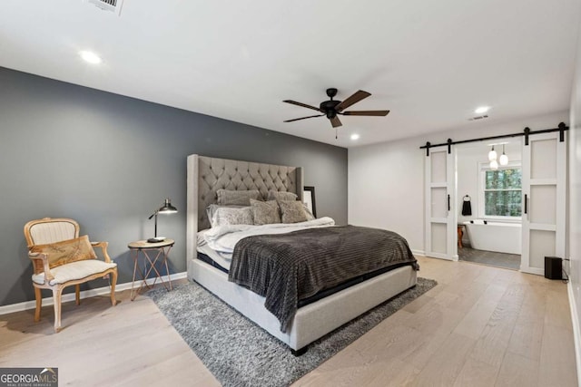 bedroom with hardwood / wood-style flooring, a barn door, ceiling fan, and ensuite bathroom