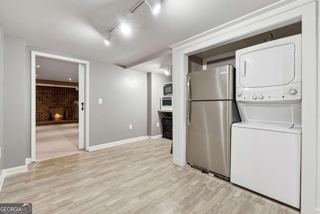 clothes washing area featuring stacked washer and dryer, rail lighting, a brick fireplace, brick wall, and light hardwood / wood-style floors