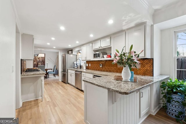 kitchen featuring white cabinetry, appliances with stainless steel finishes, a kitchen breakfast bar, kitchen peninsula, and light stone countertops