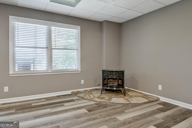 empty room with a paneled ceiling, hardwood / wood-style floors, and a wood stove