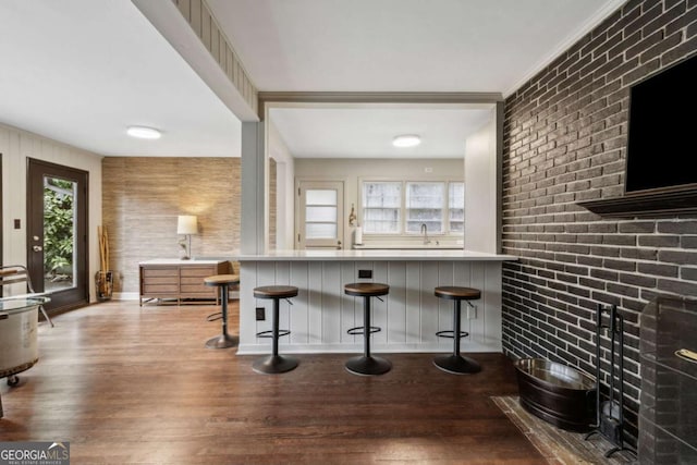 kitchen featuring a healthy amount of sunlight, a kitchen bar, brick wall, and wood-type flooring