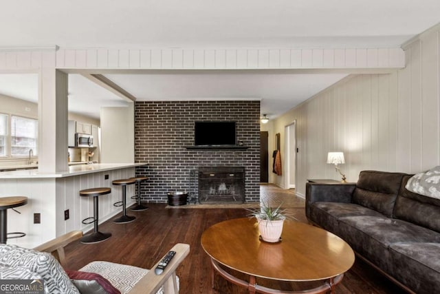 living room featuring beamed ceiling, dark wood-type flooring, sink, and a fireplace