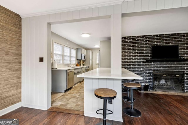 kitchen with sink, appliances with stainless steel finishes, a kitchen bar, dark hardwood / wood-style flooring, and kitchen peninsula