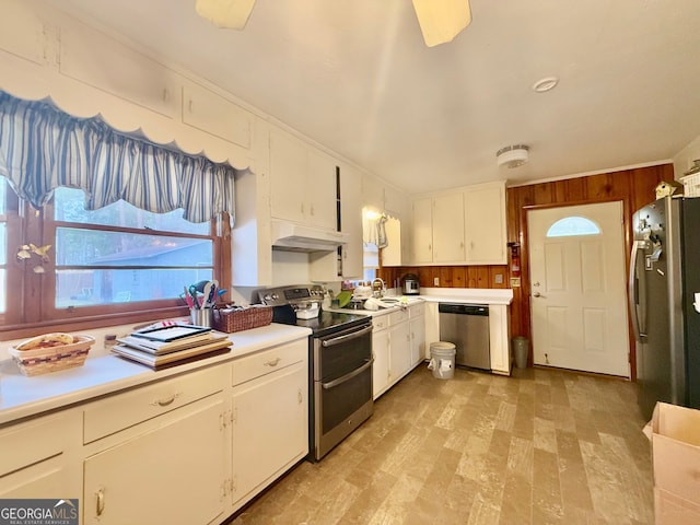 kitchen with crown molding, wood walls, stainless steel appliances, and white cabinets