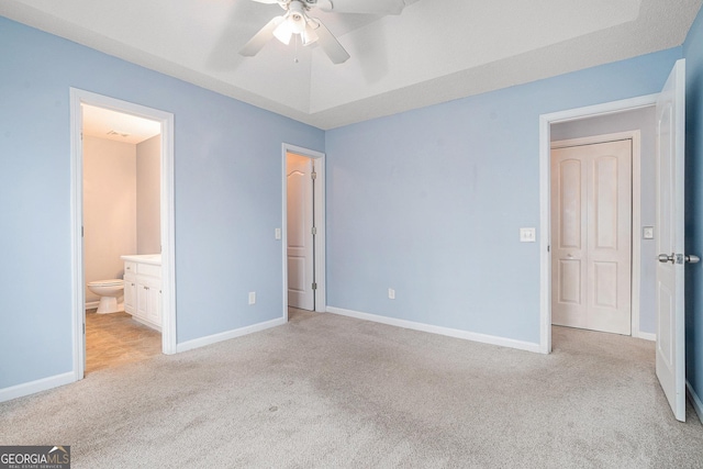 unfurnished bedroom featuring light carpet, connected bathroom, a tray ceiling, and ceiling fan