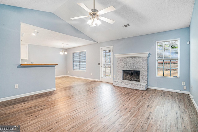 unfurnished living room with ceiling fan with notable chandelier, vaulted ceiling, a textured ceiling, and light wood-type flooring