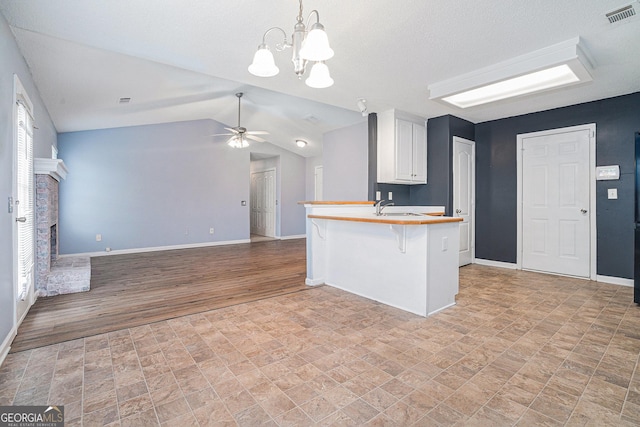 kitchen with ceiling fan with notable chandelier, white cabinets, a kitchen breakfast bar, kitchen peninsula, and a brick fireplace