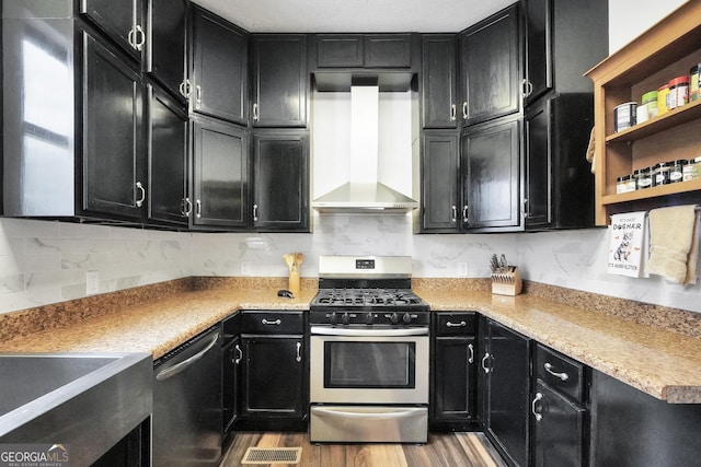 kitchen with backsplash, appliances with stainless steel finishes, light wood-type flooring, and wall chimney range hood