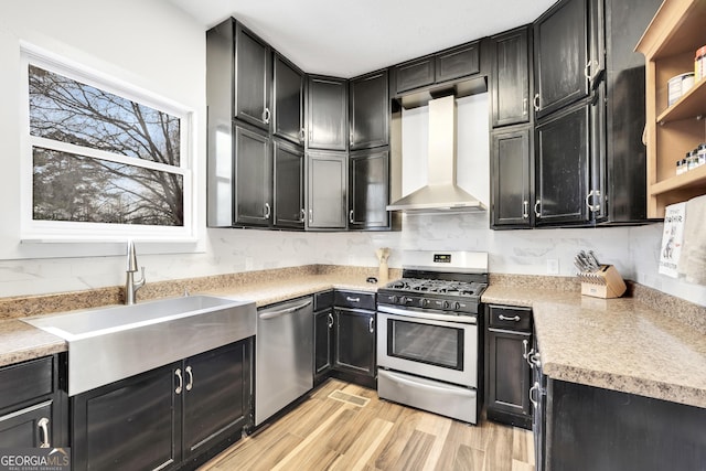 kitchen with appliances with stainless steel finishes, sink, backsplash, wall chimney range hood, and light wood-type flooring