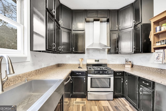 kitchen featuring wall chimney exhaust hood, sink, light wood-type flooring, stainless steel appliances, and decorative backsplash