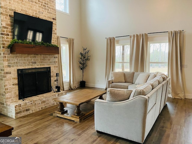 living room with wood-type flooring, a brick fireplace, and a high ceiling