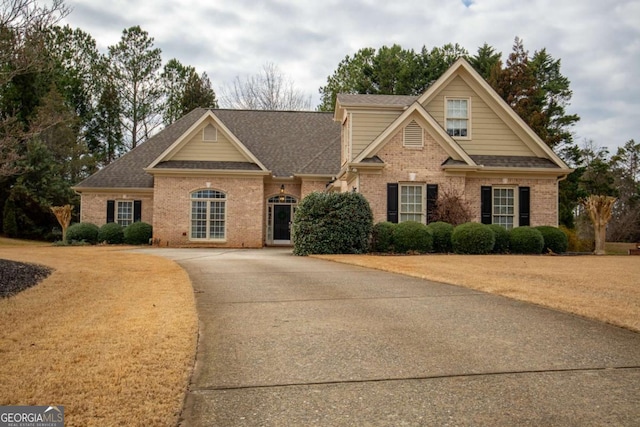 craftsman house with driveway, brick siding, roof with shingles, and a front yard