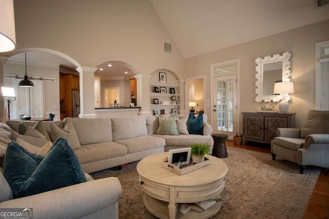 living room with decorative columns, hardwood / wood-style floors, built in features, and high vaulted ceiling