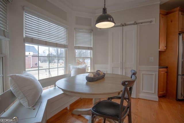 dining area with light hardwood / wood-style flooring, ornamental molding, and a barn door