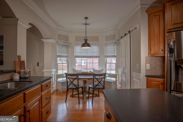 kitchen featuring decorative light fixtures, decorative columns, decorative backsplash, ornamental molding, and stainless steel refrigerator with ice dispenser