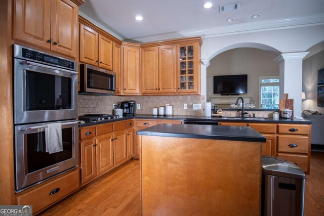 kitchen featuring appliances with stainless steel finishes, tasteful backsplash, sink, ornamental molding, and light wood-type flooring