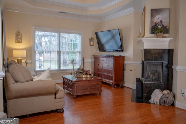 living room featuring a raised ceiling, a tile fireplace, dark hardwood / wood-style floors, and crown molding