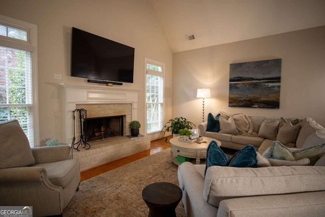 living room featuring vaulted ceiling, a brick fireplace, and hardwood / wood-style floors