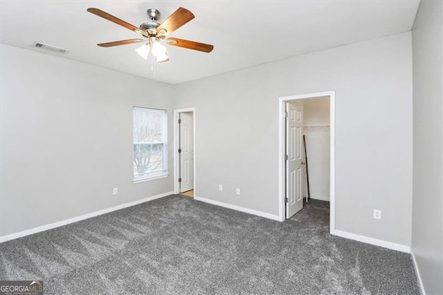 unfurnished bedroom with a walk in closet, a closet, ceiling fan, and dark colored carpet