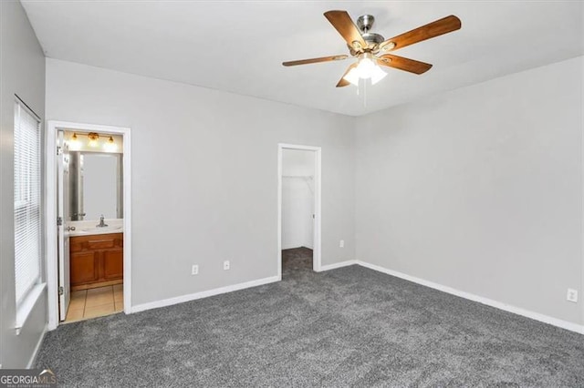 unfurnished bedroom with connected bathroom, sink, dark colored carpet, a spacious closet, and a closet