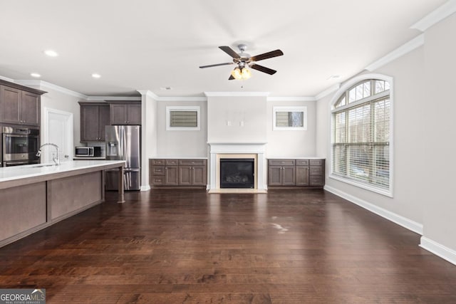 unfurnished living room featuring dark wood-type flooring, ceiling fan, ornamental molding, and sink