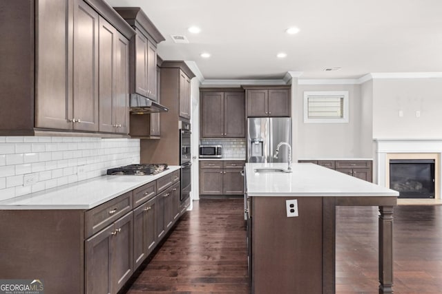 kitchen featuring dark hardwood / wood-style floors, sink, stainless steel appliances, crown molding, and a center island with sink