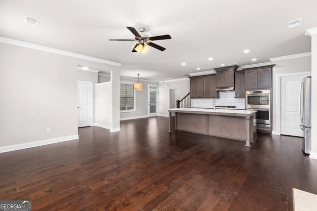 kitchen featuring dark brown cabinetry, tasteful backsplash, ceiling fan, stainless steel appliances, and a kitchen island with sink