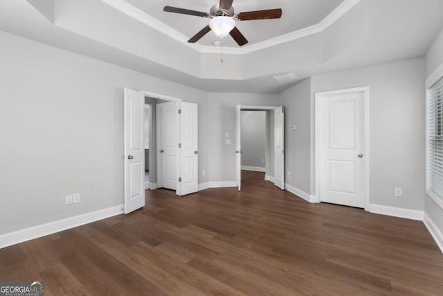 unfurnished bedroom with crown molding, ceiling fan, dark hardwood / wood-style flooring, and a tray ceiling