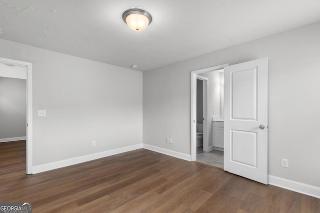 unfurnished bedroom featuring dark hardwood / wood-style floors and ensuite bath