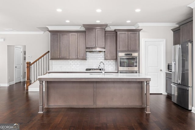 kitchen featuring stainless steel appliances, crown molding, a center island with sink, and dark brown cabinetry