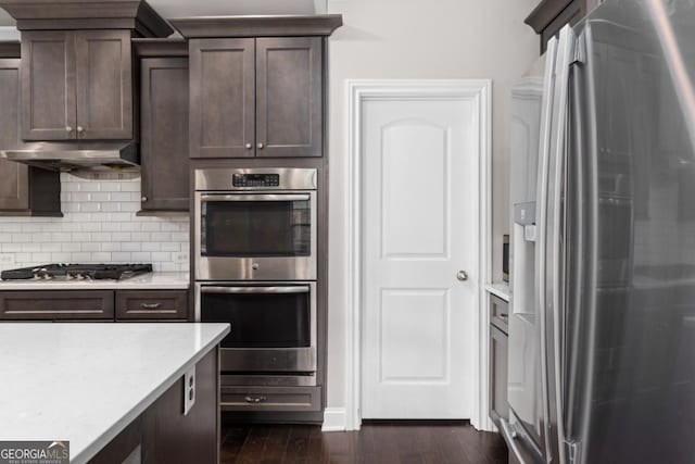 kitchen with light stone counters, dark brown cabinetry, appliances with stainless steel finishes, and dark hardwood / wood-style flooring