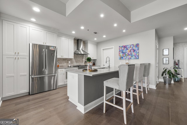 kitchen featuring wall chimney range hood, a breakfast bar area, high end fridge, white cabinetry, and a center island with sink