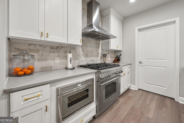 kitchen featuring wall chimney exhaust hood, white cabinetry, stainless steel range, light hardwood / wood-style floors, and decorative backsplash